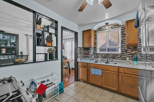 kitchen with light tile patterned floors, brown cabinetry, a sink, decorative backsplash, and light countertops