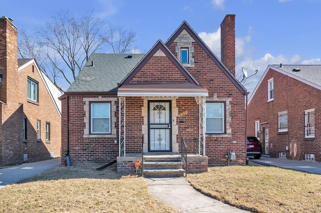 view of front facade with brick siding, a chimney, a front lawn, and roof with shingles