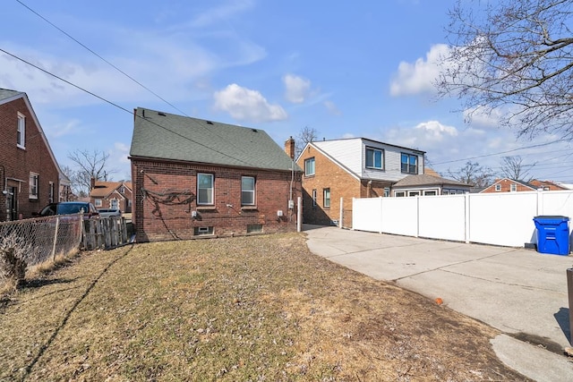 rear view of property featuring a fenced backyard, brick siding, roof with shingles, and a lawn