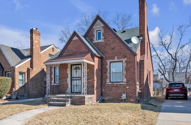 view of front facade with a shingled roof, a front lawn, brick siding, and a chimney