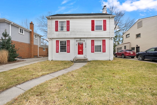 colonial home with brick siding, a front lawn, and a chimney