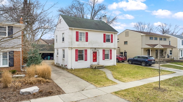 colonial home featuring brick siding, a front lawn, a chimney, and a shingled roof