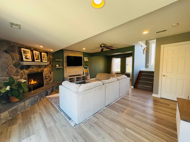 living area featuring visible vents, ceiling fan, stairs, a stone fireplace, and light wood-style floors