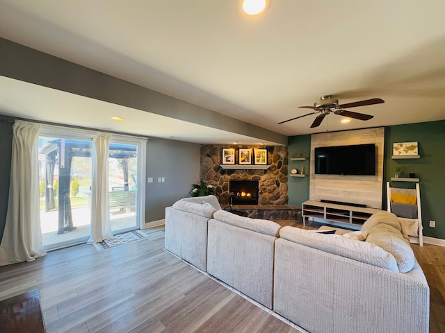 living area featuring a stone fireplace, ceiling fan, baseboards, and wood finished floors