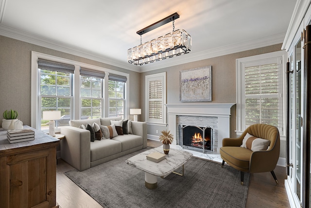 living room featuring a notable chandelier, wood finished floors, a warm lit fireplace, and ornamental molding