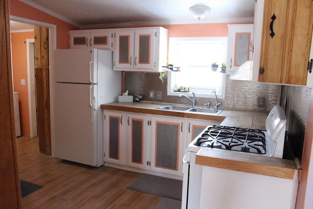 kitchen featuring dark wood-type flooring, ornamental molding, a sink, white appliances, and light countertops