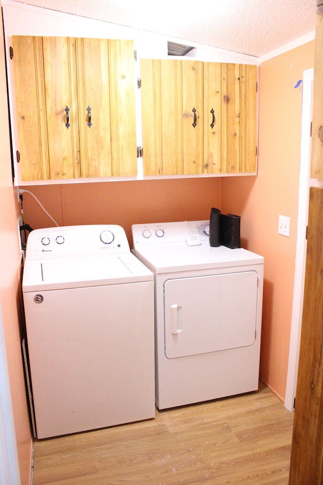 clothes washing area featuring visible vents, a textured ceiling, washing machine and dryer, cabinet space, and light wood-style floors