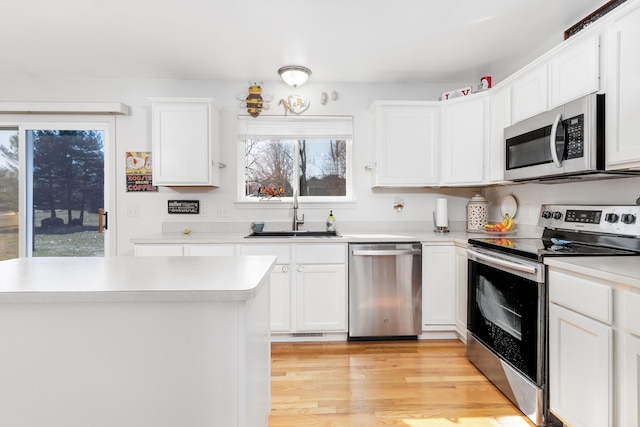 kitchen featuring light wood finished floors, a sink, light countertops, white cabinets, and appliances with stainless steel finishes