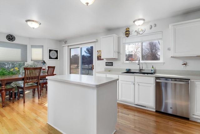 kitchen with light wood finished floors, a kitchen island, dishwasher, light countertops, and a sink