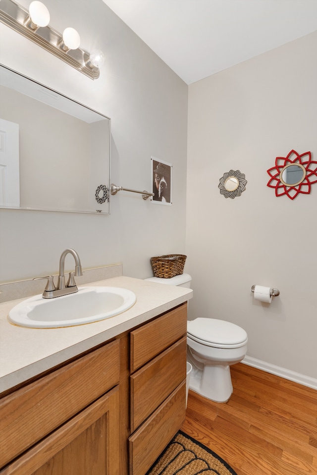 half bath featuring vanity, toilet, wood finished floors, and baseboards