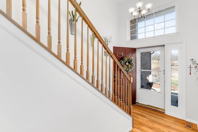 foyer entrance with visible vents, a chandelier, stairs, a towering ceiling, and wood finished floors