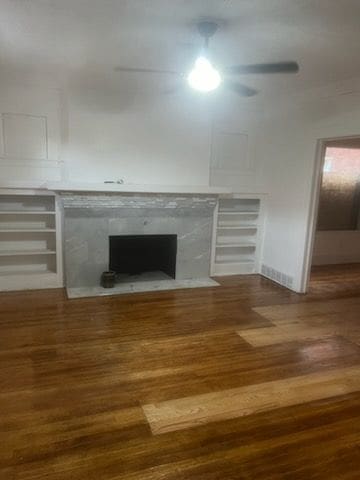 unfurnished living room featuring a fireplace with flush hearth, ceiling fan, and wood finished floors