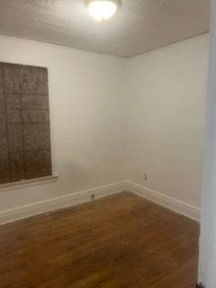 empty room with a textured ceiling, baseboards, and wood finished floors