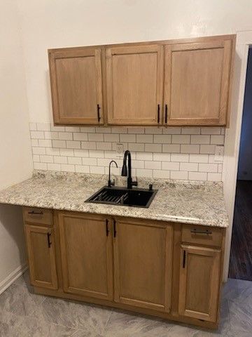 kitchen featuring light stone countertops, baseboards, backsplash, and a sink