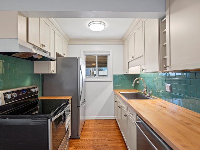 kitchen with wooden counters, a sink, light wood-style floors, under cabinet range hood, and appliances with stainless steel finishes