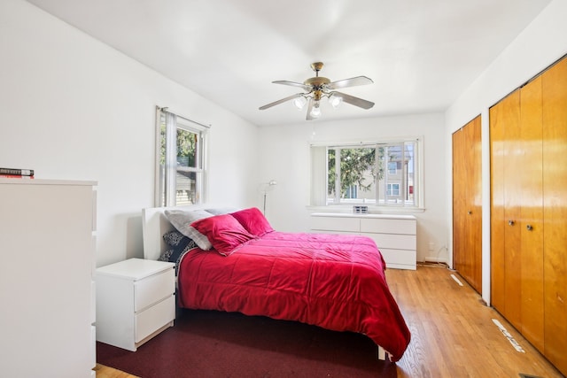 bedroom with multiple windows, light wood-type flooring, two closets, and ceiling fan