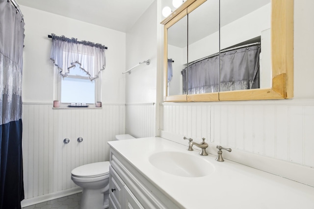 bathroom featuring a wainscoted wall, toilet, and vanity