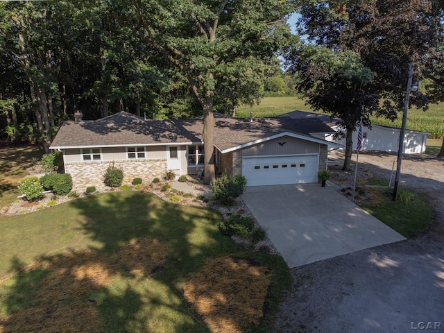 ranch-style home featuring a front yard, an attached garage, stone siding, and driveway