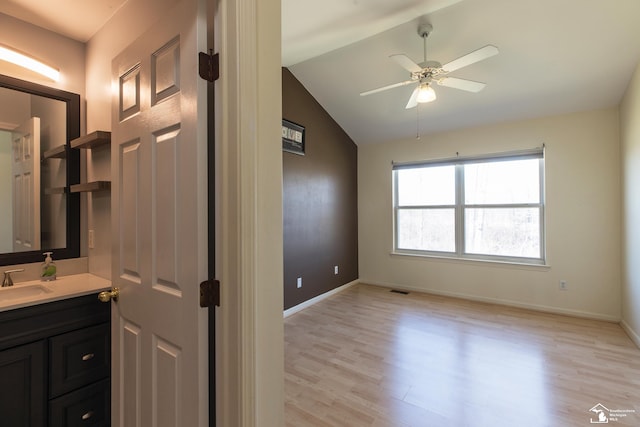 interior space with vanity, a ceiling fan, wood finished floors, baseboards, and vaulted ceiling