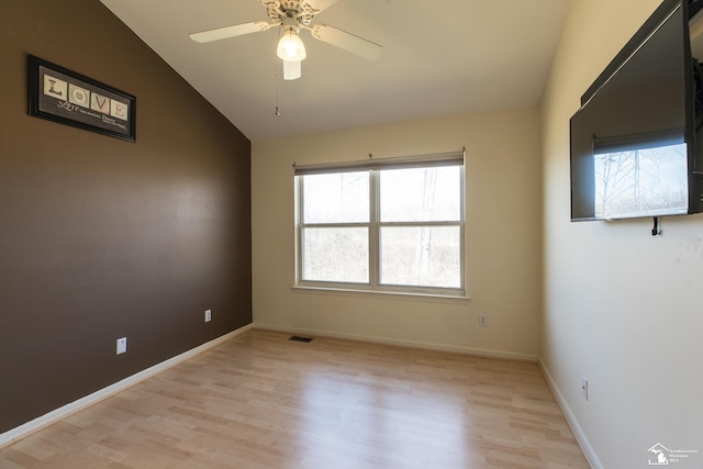 empty room featuring visible vents, baseboards, light wood-style floors, and vaulted ceiling