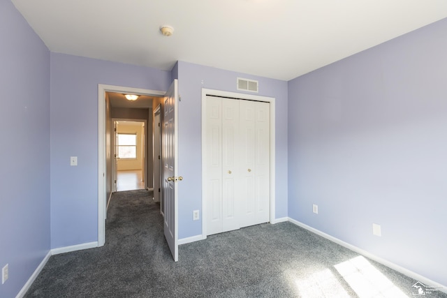 unfurnished bedroom featuring a closet, visible vents, dark carpet, and baseboards