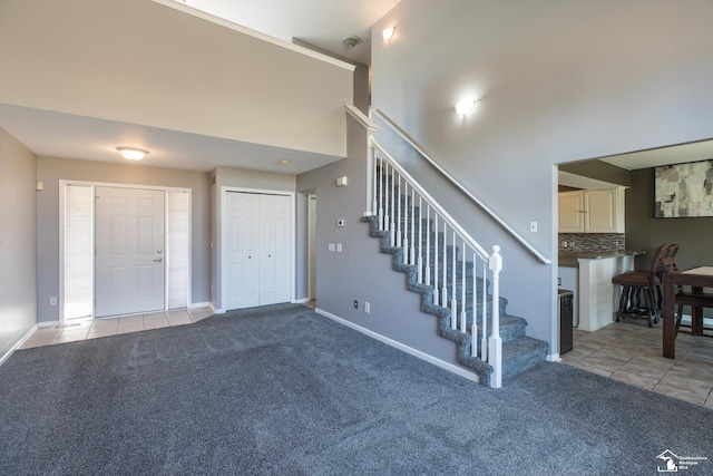 interior space with tile patterned floors, baseboards, carpet floors, and a high ceiling