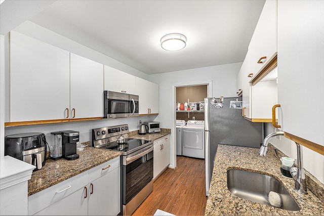 kitchen with a sink, wood finished floors, white cabinetry, stainless steel appliances, and separate washer and dryer