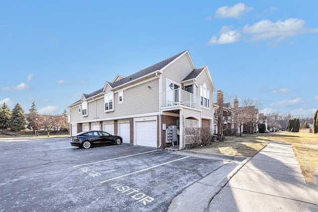 view of side of property with brick siding, community garages, and a balcony