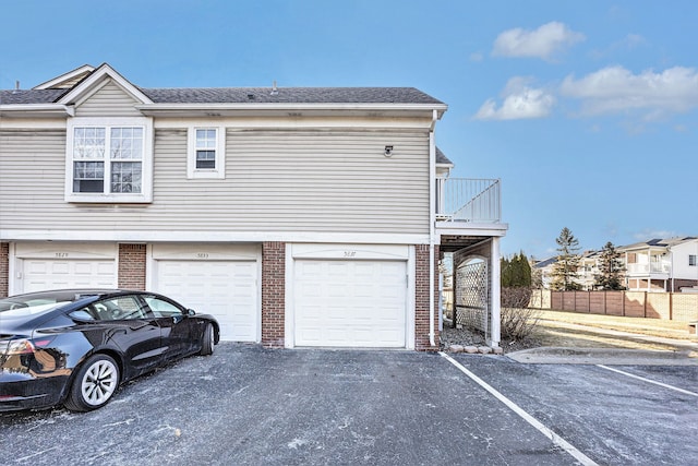 exterior space featuring a garage, fence, brick siding, and roof with shingles