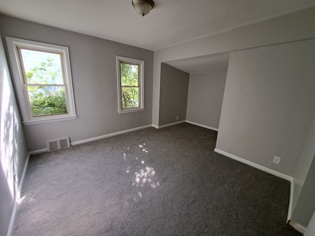 unfurnished room with a wealth of natural light, visible vents, dark carpet, and baseboards