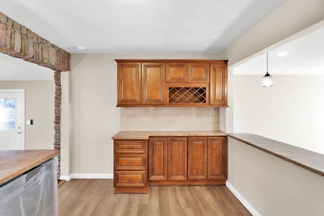 kitchen featuring brown cabinets, light wood-style floors, decorative columns, baseboards, and dishwasher