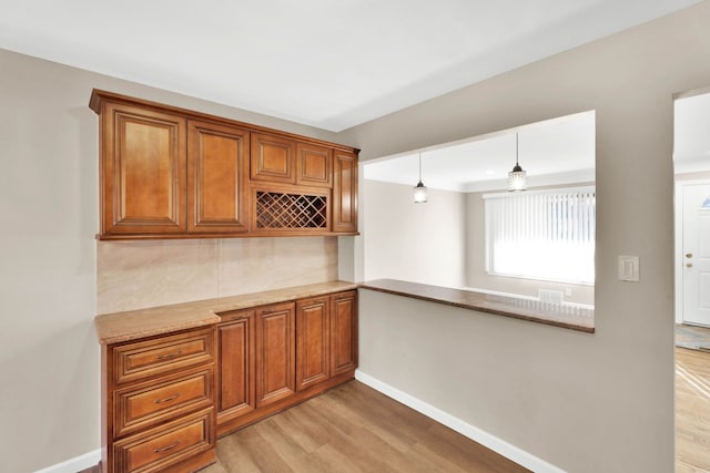 kitchen with tasteful backsplash, baseboards, decorative light fixtures, light wood-type flooring, and brown cabinets