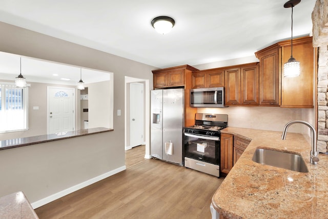 kitchen featuring pendant lighting, light stone counters, appliances with stainless steel finishes, light wood-style floors, and a sink