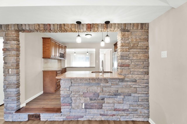 kitchen with brown cabinets, a peninsula, wood finished floors, refrigerator, and a sink