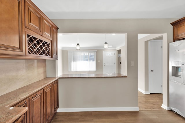 kitchen featuring brown cabinetry, decorative backsplash, fridge with ice dispenser, and wood finished floors