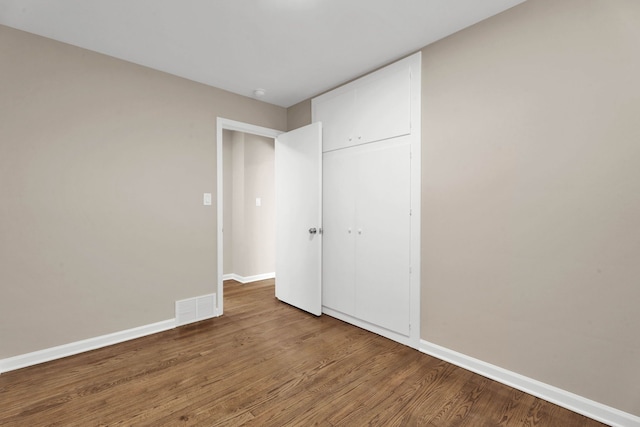 unfurnished bedroom with a closet, visible vents, baseboards, and wood finished floors