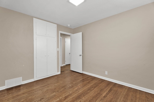 unfurnished bedroom featuring wood finished floors, visible vents, a closet, and baseboards