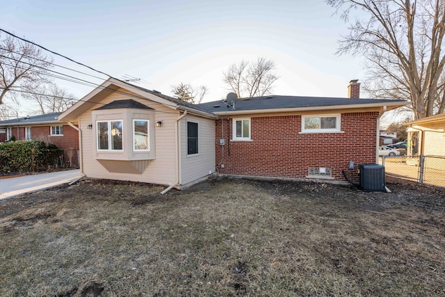 rear view of house with cooling unit, brick siding, a chimney, and fence