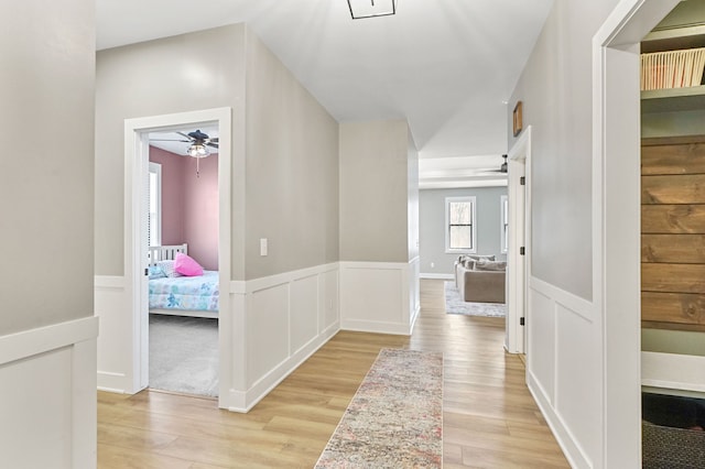 hall with a wainscoted wall, a decorative wall, and light wood finished floors