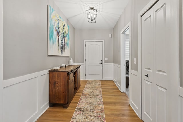 entryway with a decorative wall, a notable chandelier, light wood-style floors, and wainscoting