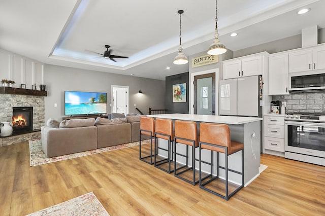 kitchen with a tray ceiling, a kitchen breakfast bar, white cabinetry, white appliances, and light wood finished floors