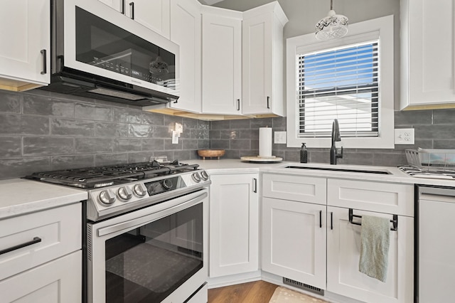 kitchen featuring stainless steel gas range oven, backsplash, light countertops, white cabinetry, and a sink