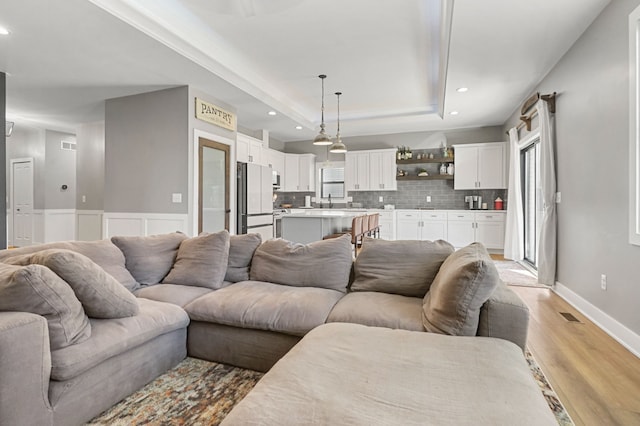 living room featuring recessed lighting, baseboards, a raised ceiling, and light wood finished floors