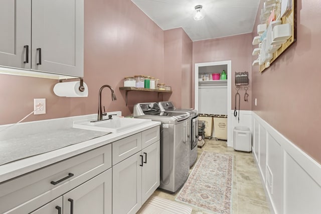 washroom with independent washer and dryer, a sink, cabinet space, wainscoting, and a decorative wall