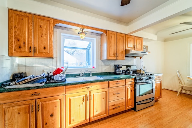 kitchen featuring stainless steel gas range oven, ceiling fan, under cabinet range hood, light wood-style floors, and a sink