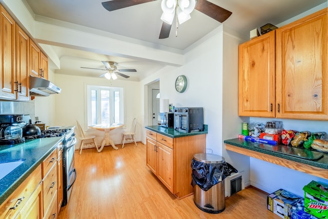 kitchen featuring dark countertops, stainless steel gas range, light wood-type flooring, and under cabinet range hood