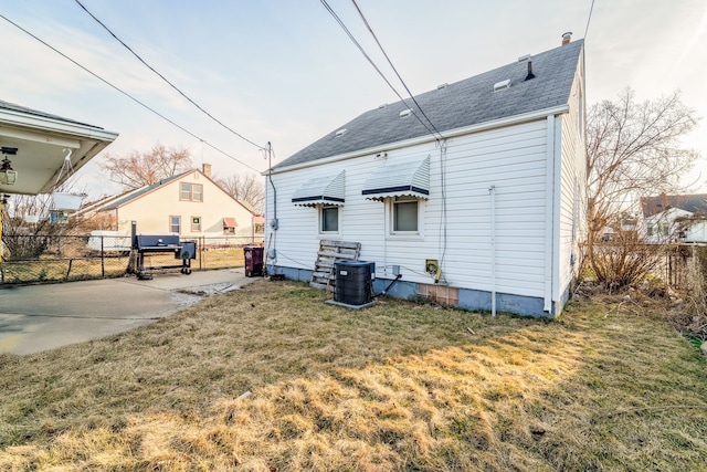 back of property with a lawn, central AC unit, a shingled roof, and fence