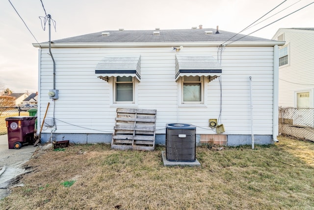 back of property featuring cooling unit, a shingled roof, a yard, and fence