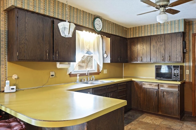 kitchen with a peninsula, dark brown cabinetry, wallpapered walls, light countertops, and a sink