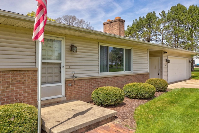 view of exterior entry featuring brick siding, a garage, a chimney, and concrete driveway